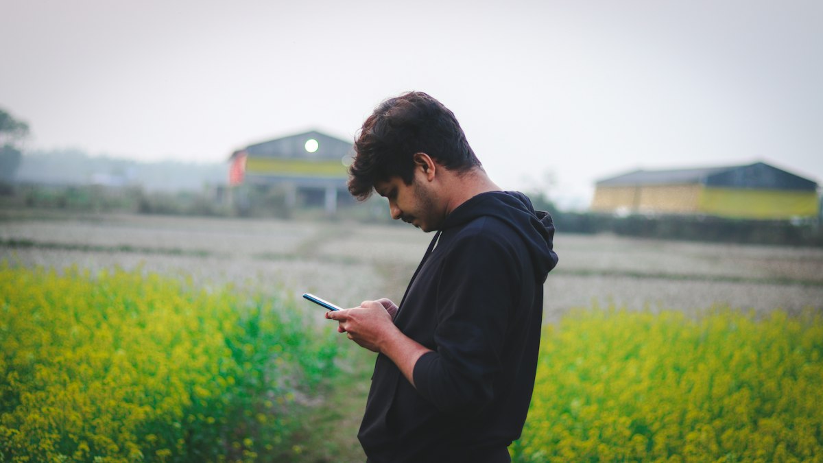 A young man reading his phone in a green field